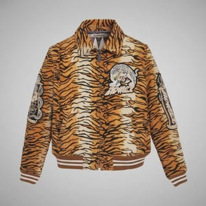 May include: A tan and brown tiger-striped bomber jacket with a zip-up front and a brown and white striped collar and cuffs. The jacket features embroidered patches of a tiger and other designs.