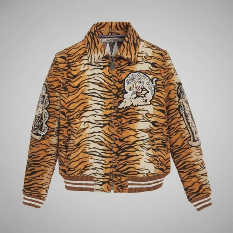 May include: A tan and brown tiger-striped bomber jacket with a zip-up front and a brown and white striped collar and cuffs. The jacket features embroidered patches of a tiger and other designs.