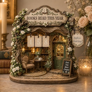 May include: A miniature bookstore display titled BOOKS READ THIS YEAR with the number 158 displayed on hanging tags. The structure features a green door, a small armchair, a table, and a sign reading Sophia's bookshop and Just One More Chapter.