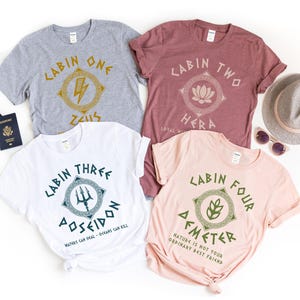 Può includere: Quattro magliette in grigio, bordeaux, bianco e rosa, ognuna con un design e un testo unici. Le magliette presentano grafiche ispirate alla mitologia greca e le parole "LABIN ONE ZEUS", "LABIN TWO HERA", "LABIN THREE POSEIDON" e "LABIN FOUR DEMETER".