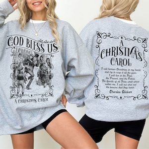 Może przedstawiać: Jasnoszara bluza z okrągłym dekoltem i czarnymi nadrukami graficznymi. Przód przedstawia ilustrację w stylu vintage z napisem GOD BLESS US EVERYONE! A CHRISTMAS CAROL. Tył zawiera napis A CHRISTMAS CAROL oraz cytat autorstwa Charlesa Dickensa.