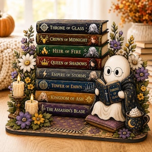 Könnte beinhalten: Ein dekoratives Display mit einem Stapel von acht Büchern mit den Titeln Throne of Glass, Crown of Midnight, Heir of Fire, Queen of Shadows, Empire of Storms, Tower of Dawn, Kingdom of Ash und The Assassin's Blade sowie einer lesenden Geisterfigur.