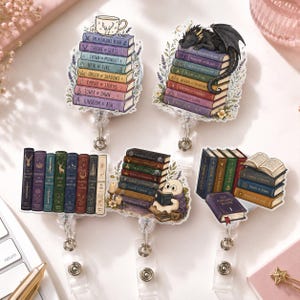 May include: Five badge reels featuring book-themed designs. Two show stacks of books with titles like Throne of Glass, one with a cup, one with a dragon. Others show a row of books, a ghost reading, and an open book atop a stack of volumes.