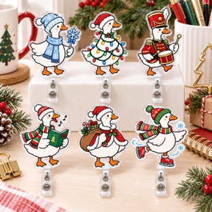 Puede incluir: Seis portatarjetas de acrílico con gansos blancos vestidos de Navidad. Los gansos están disfrazados de viajero invernal, árbol con luces, tamborilero, cantante de villancicos, Papá Noel con saco de regalos y patinador con patines rojos.