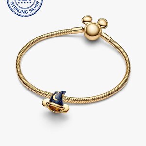 K&ouml;nnte beinhalten: Ein goldfarbenes Armband mit einem Charm in Form eines Zaubererhuts. Der Hut ist dunkelblau mit einem Mond- und Sternenmuster. Das Armband hat einen Mickey Mouse-Kopfverschluss und ein Schlangenketten-Design. Das Bild enth&auml;lt auch einen 925 Sterling Silver Stempel.