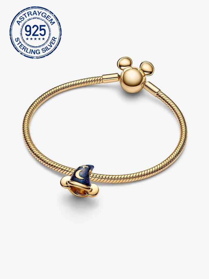 K&ouml;nnte beinhalten: Ein goldfarbenes Armband mit einem Charm in Form eines Zaubererhuts. Der Hut ist dunkelblau mit einem Mond- und Sternenmuster. Das Armband hat einen Mickey Mouse-Kopfverschluss und ein Schlangenketten-Design. Das Bild enth&auml;lt auch einen 925 Sterling Silver Stempel.