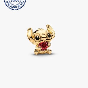 May include: A gold-coloured charm depicting a cartoon character holding a red heart-shaped gem. The charm has black eyes and a textured surface. The charm is stamped with "925 STERLING SILVER".