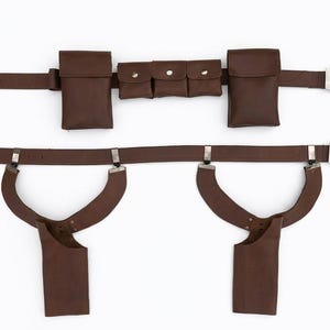May include: Brown leather utility belt with multiple pouches and a silver-colored buckle. The belt features two large pouches, three smaller pouches, and two holster-style attachments. The belt is designed for carrying items.