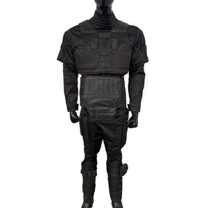 Pu&ograve; includere: Un costume tattico nero esposto su un manichino. L'outfit include un top a maniche corte, una protezione per il petto e l'addome, pantaloni e stivali. Il costume &egrave; progettato con pi&ugrave; pannelli e texture.