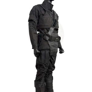 Pu&ograve; includere: Completo tattico interamente nero, composto da giacca, pantaloni e stivali. La giacca ha un colletto alto e spalline. L'outfit presenta tasche e cinghie multiple, con una cintura e una tracolla. Gli stivali hanno fibbie multiple.
