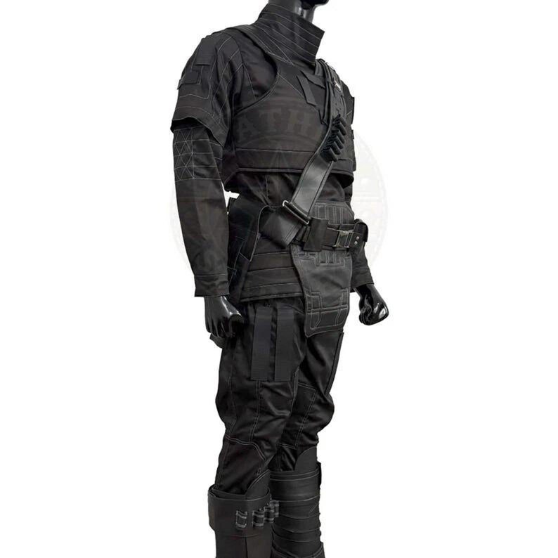 Pu&ograve; includere: Completo tattico interamente nero, composto da giacca, pantaloni e stivali. La giacca ha un colletto alto e spalline. L'outfit presenta tasche e cinghie multiple, con una cintura e una tracolla. Gli stivali hanno fibbie multiple.