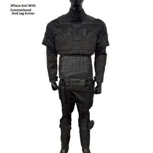 Pu&ograve; includere: Un completo nero a 3 pezzi con panciera e armatura per le gambe. Il completo include un top a maniche corte, un paraseno e addominale e pantaloni con armatura per le gambe. Il testo "3Piece Suit With Cummerbund And Leg Armor" &egrave; visibile.