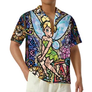 May include: A short-sleeve button-down shirt featuring a vibrant, multicolored stained-glass pattern. The design displays a central illustration of a fairy with blonde hair and green clothing, surrounded by clocks, keys, and geometric shapes.