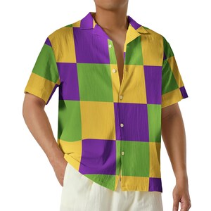 May include: Short-sleeved button-down shirt with a checkerboard pattern in green, purple, and yellow. The shirt has a classic collar and is unbuttoned at the top. The garment is made of a lightweight fabric.