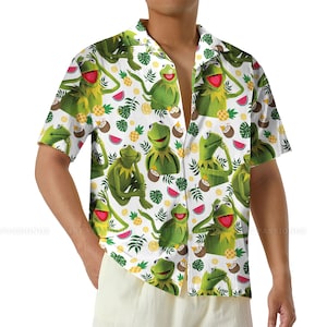 May include: Short-sleeved button-down shirt with a white background and a repeating pattern of Kermit the Frog, pineapples, coconuts, and watermelon slices. The shirt has a relaxed fit and a classic collar.