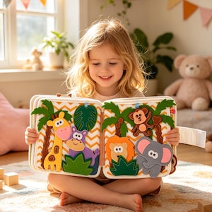 May include: A child holds an open felt book with colorful jungle animal illustrations. The book features a giraffe, hippo, lion, elephant, and monkey. The background includes a window, toys, and a patterned rug.