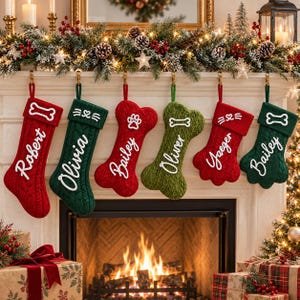 May include: A collection of six hanging Christmas stockings in red and green cable knit patterns. Some are shaped like traditional stockings, while others are shaped like bones or paws. Each features white embroidered names and pet icons.