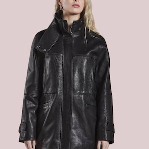May include: A black leather jacket with a high collar and a textured finish. The jacket has a zip closure, pockets, and buttoned cuffs. The model is wearing black pants.