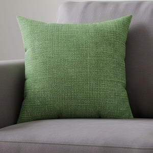 May include: A square throw cushion featuring a vibrant green fabric cover with a visible woven texture. The cushion has a simple, clean design with straight edges and a uniform colour throughout, providing a solid block of colour for a seating area.