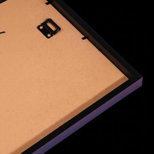 a close-up view of a wooden frame with a black metal hook or bracket attached to it, set against a dark background.
