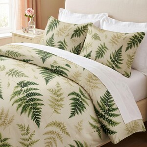 May include: A bedding set featuring a duvet cover and two pillow shams with a cream-colored base and a repeating pattern of dark green and muted light green fern leaves. The set includes a solid white flat sheet folded over the top edge.