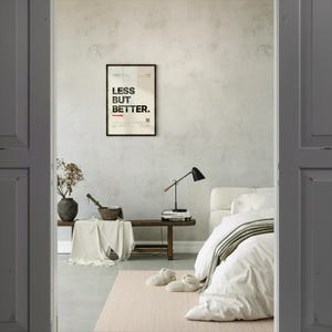 a bedroom with a bed, a nightstand, and a framed poster on the wall. The poster has the text "LESS BUT BETTER" written on it.