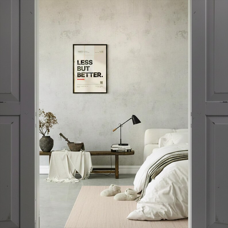 a bedroom with a bed, a nightstand, and a framed poster on the wall. The poster has the text "LESS BUT BETTER" written on it.