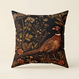 May include: A square throw cushion featuring a black background with a detailed illustration of a pheasant bird standing among various golden-brown wildflowers, ferns, and foliage. The bird has brown, orange, and white plumage.
