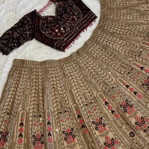 May include: A beige and maroon embroidered formal outfit. The ensemble includes a long-sleeved maroon top with intricate sequin and beadwork, and a matching beige skirt with floral and geometric patterns.