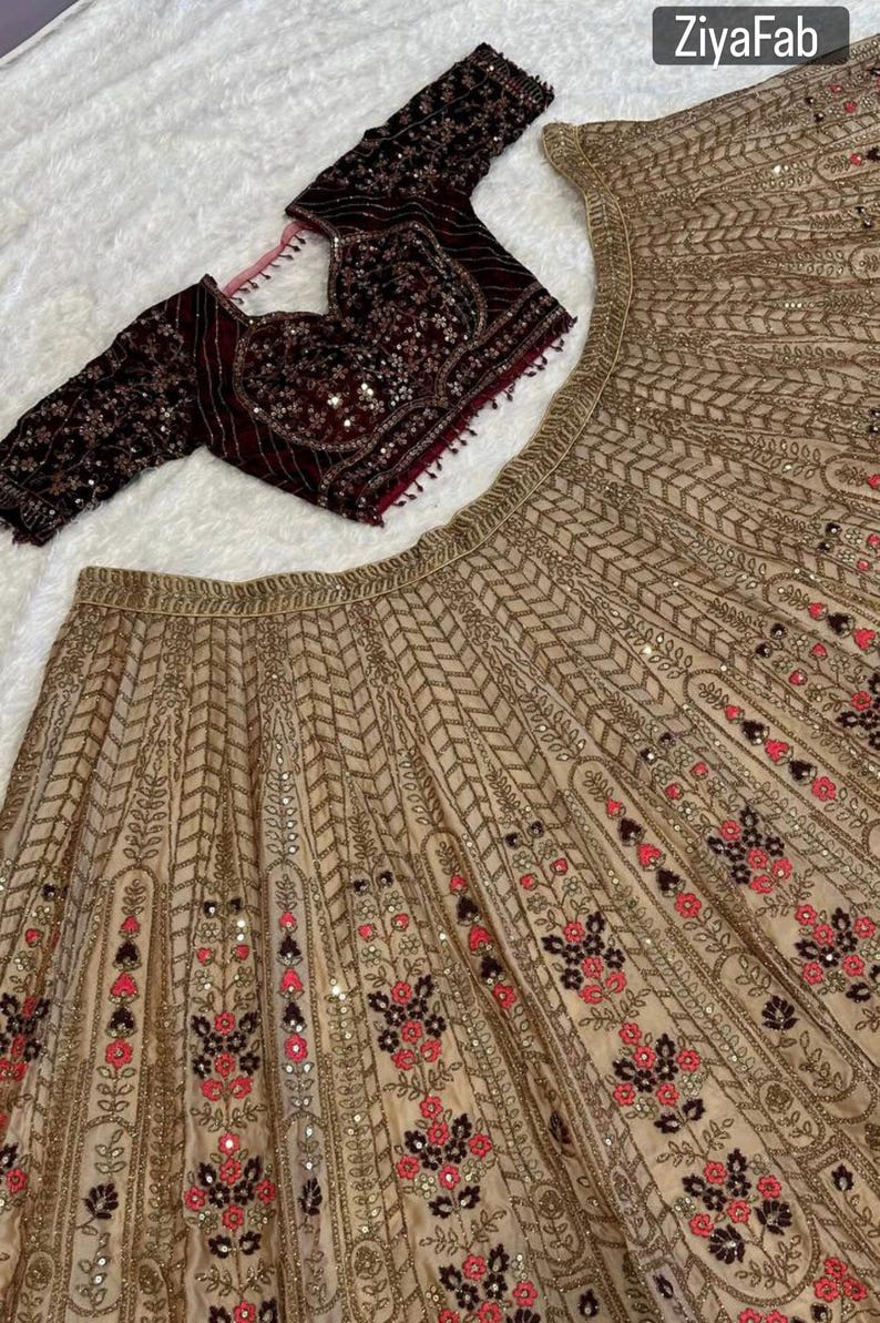 May include: A beige and maroon embroidered formal outfit. The ensemble includes a long-sleeved maroon top with intricate sequin and beadwork, and a matching beige skirt with floral and geometric patterns.