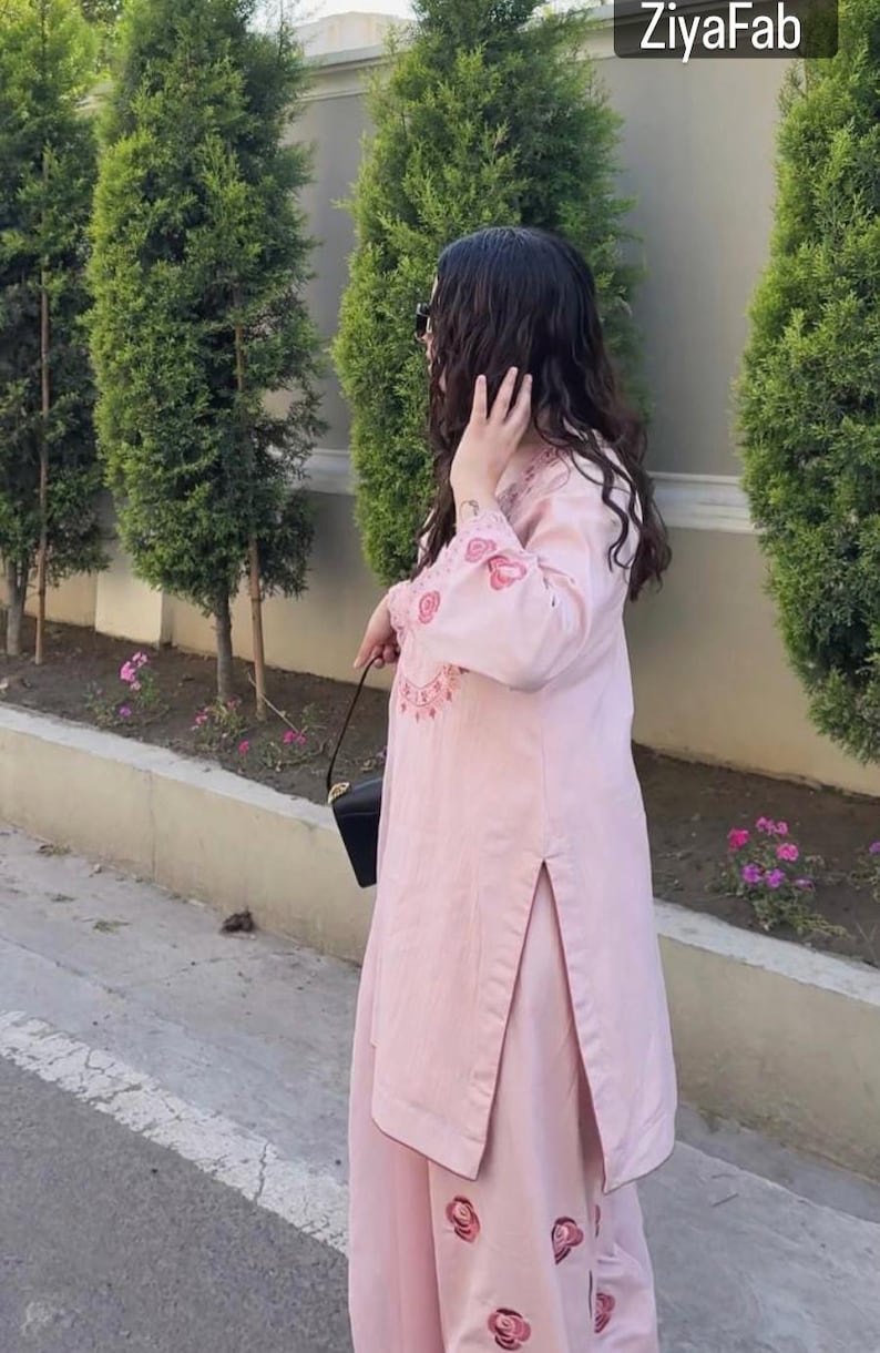 May include: A light pink two-piece outfit with floral embroidery. The long-sleeved top and matching pants feature decorative floral patterns. The outfit is worn with a black purse. The brand name "ZiyaFab" is visible in the top right corner.