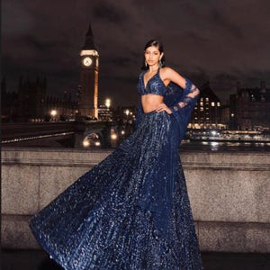 Puede incluir: Un vestido de noche azul marino con lentejuelas con un top y un chal a juego. El atuendo se usa frente al horizonte de Londres por la noche, con la torre del reloj del Big Ben al fondo. La marca "ZiyaFab" está en la esquina superior derecha.