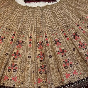 May include: A beige and burgundy formal outfit. The skirt features intricate gold embroidery with floral patterns in pink and black. The top is a burgundy velvet with sequin embellishments. The brand name "ZiyaFab" is visible.