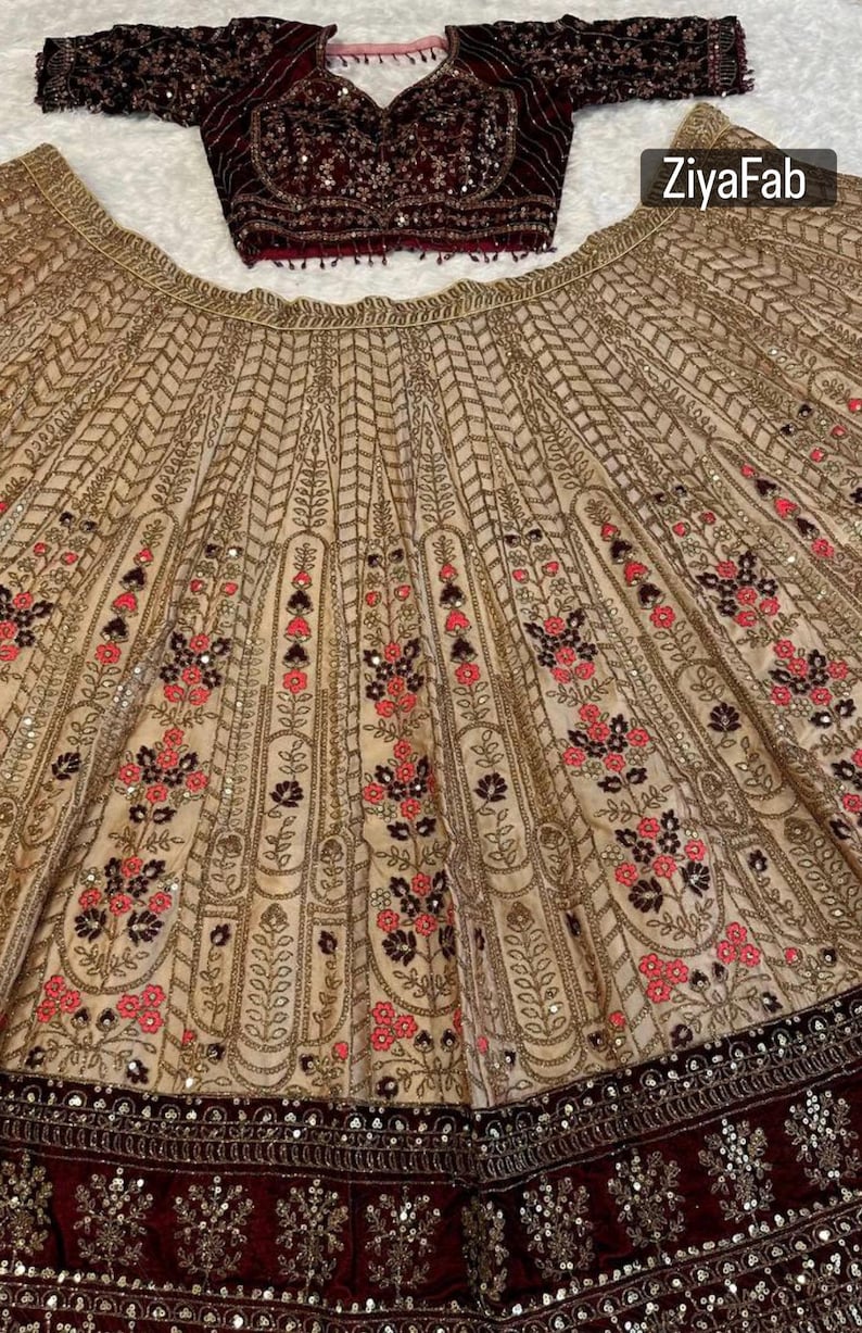 May include: A beige and burgundy formal outfit. The skirt features intricate gold embroidery with floral patterns in pink and black. The top is a burgundy velvet with sequin embellishments. The brand name "ZiyaFab" is visible.