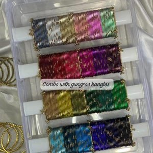 May include: A clear plastic container holds four sets of colorful bangles. Each set is a different color, including gold, pink, green, and blue. The text "Combo with gungroo bangles" is visible. The brand name "ZiyaFab" is in the top right corner.
