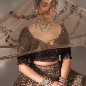 May include: An ornate, gold-toned bridal ensemble. The outfit includes a heavily embellished crop top, a full skirt, and a sheer veil with decorative trim. The model is wearing a matching necklace, bracelets, and rings. The brand name "ZiyaFab" is visible.