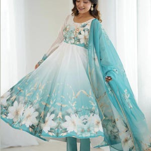 May include: An Anarkali dress with a white bodice and a flowing skirt in a blue and white floral print. The dress is paired with a matching light blue dupatta and trousers. The floral design features large white flowers. The text "ZiyaFab" is in the top right corner.
