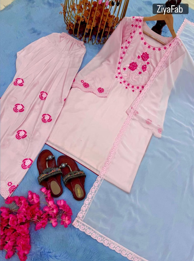 May include: A light pink embroidered salwar kameez set with matching pants and a sheer dupatta. The set features floral embroidery and lace trim. A pair of maroon sandals with decorative embellishments are also present.