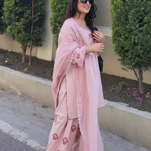 May include: A light pink salwar kameez set. The outfit includes a tunic, pants, and a scarf. The tunic and pants feature floral embroidery. The set is made of a lightweight fabric. The brand name "ZiyaFab" is visible in the top right corner.