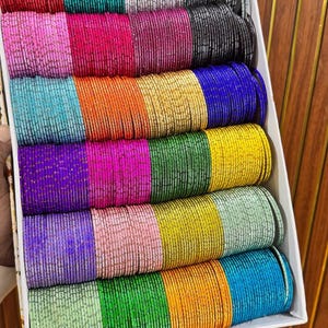 May include: A white box containing rows of thin, textured bangles in various colors including red, teal, silver, gray, pink, black, blue, orange, gold, purple, green, yellow, and light green. The text ZiyaFab is printed in the top right corner.