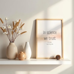 Può includere: Una stampa incorniciata con la scritta "In science we trust" è appoggiata su una mensola bianca accanto a vasi e a una pigna decorativa. La stampa ha una cornice in legno chiaro e uno sfondo in stile acquerello.