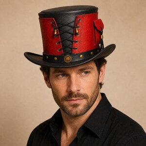 May include: A top hat featuring a black crown and brim with a red mid-section. The red portion includes black lace-up detailing with brass-coloured eyelets and a small side pocket. A black hatband with brass studs and a central gear-shaped emblem.
