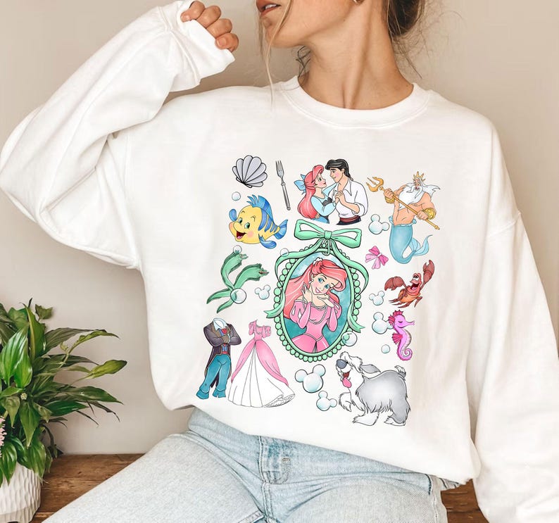 Pu&ograve; includere: Felpa bianca con illustrazioni colorate di personaggi ed elementi di un popolare film d'animazione. Il design include Ariel, Flounder, Sebastian, il Principe Eric, Re Tritone e altre immagini iconiche. Un capo d'abbigliamento comodo e casual.