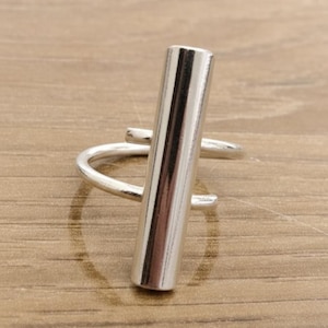Peut inclure: Une bague argentée avec un design de barre rectangulaire verticale. La bague présente une esthétique simple et moderne, avec une finition polie. La bague est faite d'un matériau métallique brillant.