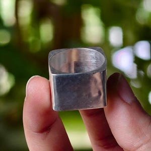 Peut inclure: Une bague argentée massive présentant une bande extérieure de forme carrée distincte avec une surface métallique lisse et réfléchissante et une ouverture intérieure circulaire, arborant un design géométrique épuré aux bords polis.