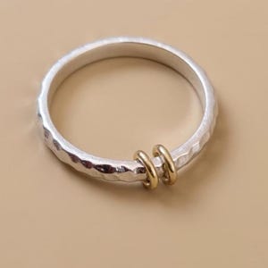 Könnte beinhalten: Ein Set aus drei Keramikbechern mit gesprenkelter, matter Oberfläche. Die Becher sind in Creme-, Hellgrau- und Dunkelgrautönen gehalten. Jeder Becher hat ein schlichtes, minimalistisches Design, ideal für Kaffee oder Tee.