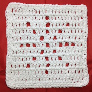 May include: A square, white crocheted washcloth with a repeating openwork pattern. The washcloth is made of thick, textured yarn and has a solid border. The openwork design creates small, evenly spaced holes throughout the cloth.