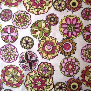 Könnte beinhalten: Ein Stoffmuster mit einem sich wiederholenden Design aus stilisierten floralen Medaillons in Rosa, Grün, Gelb und Braun. Die Blumen sind auf einem weißen Hintergrund angeordnet und erzeugen einen lebendigen Stoff.