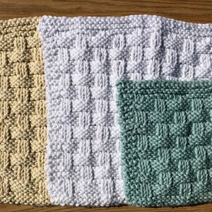 May include: Three knitted dishcloths in different colors: beige, white, and green. The dishcloths are made with a woven stitch pattern.