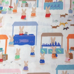 May include: A repeating pattern on white fabric depicting cartoon bunnies at market stalls. The bunnies are selling flowers, fish, and produce. Dachshunds and other dogs are also present in the scene.